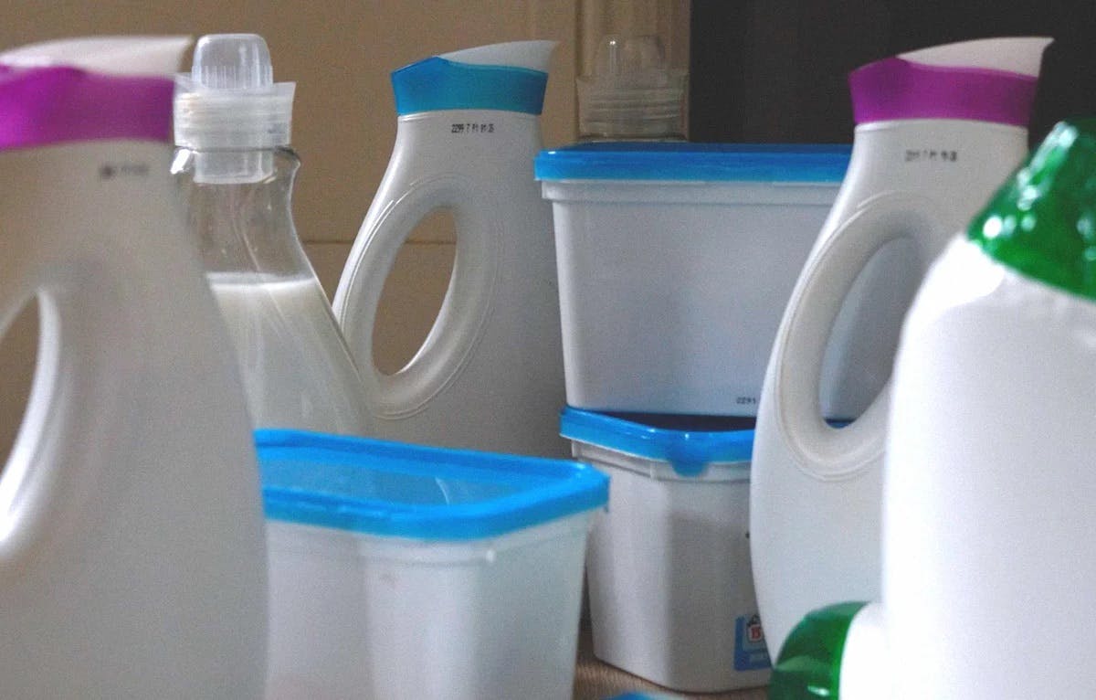 des bouteilles et boîtes blanches de lessive en plastique à usage unique sur une table en bois.