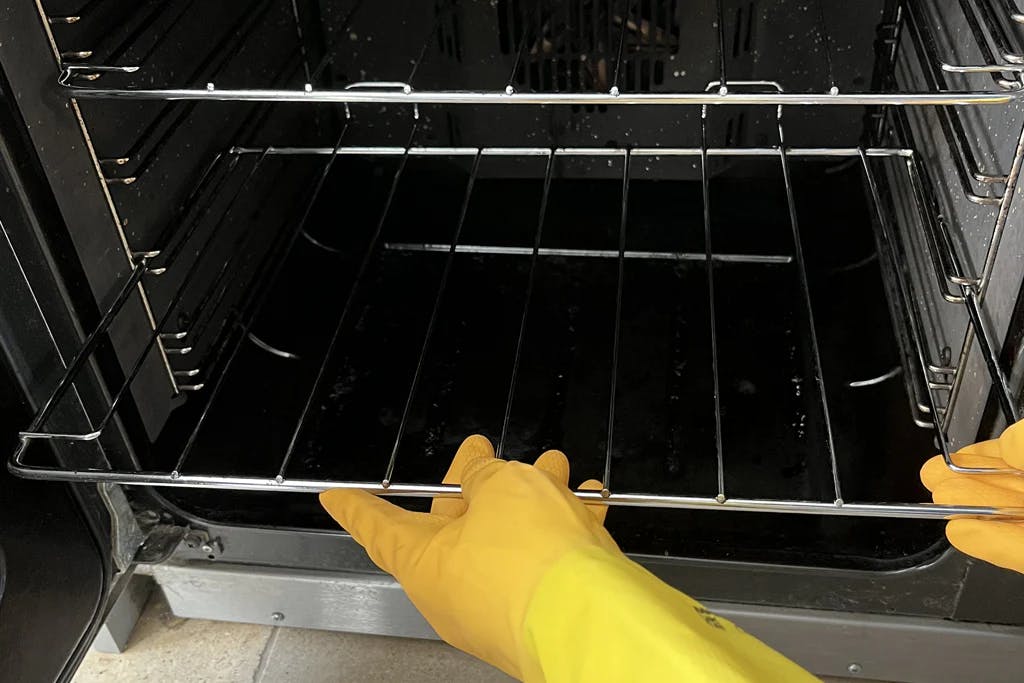 hands wearing rubber gloves putting shiny oven shelves into oven