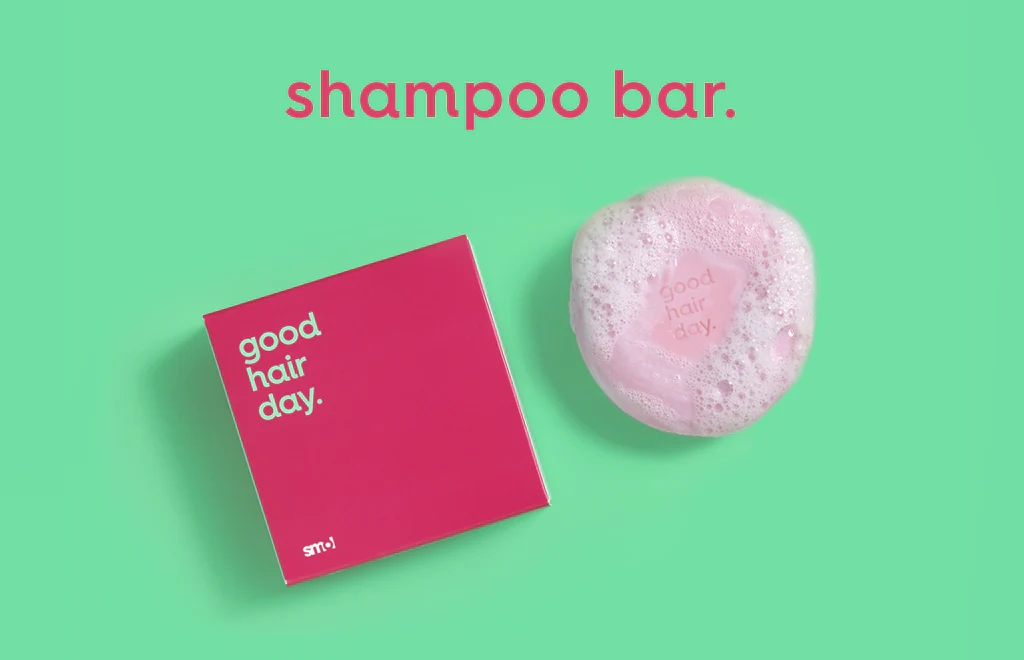 smol shampoo bar with suds alongside its pink packaging