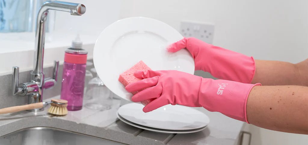 hands wearing smol plastic-free rubber gloves washing a plate next to a sink