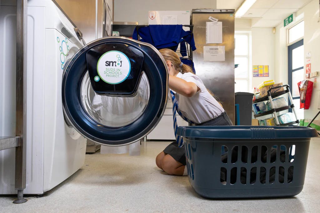 washer-dryer installed in a school with a 'smol suds in schools project' sticker on the door