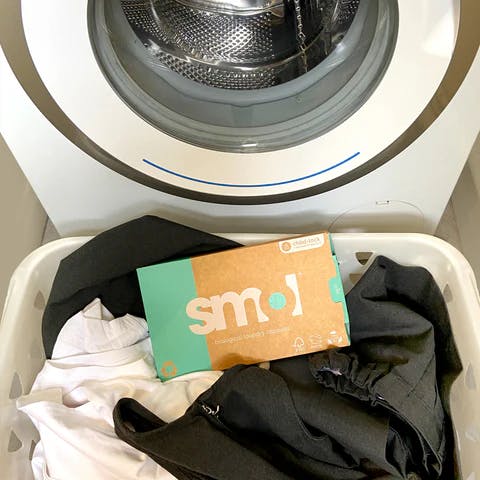 laundry basket with school clothes inside with a box of smol laundry capsules on top