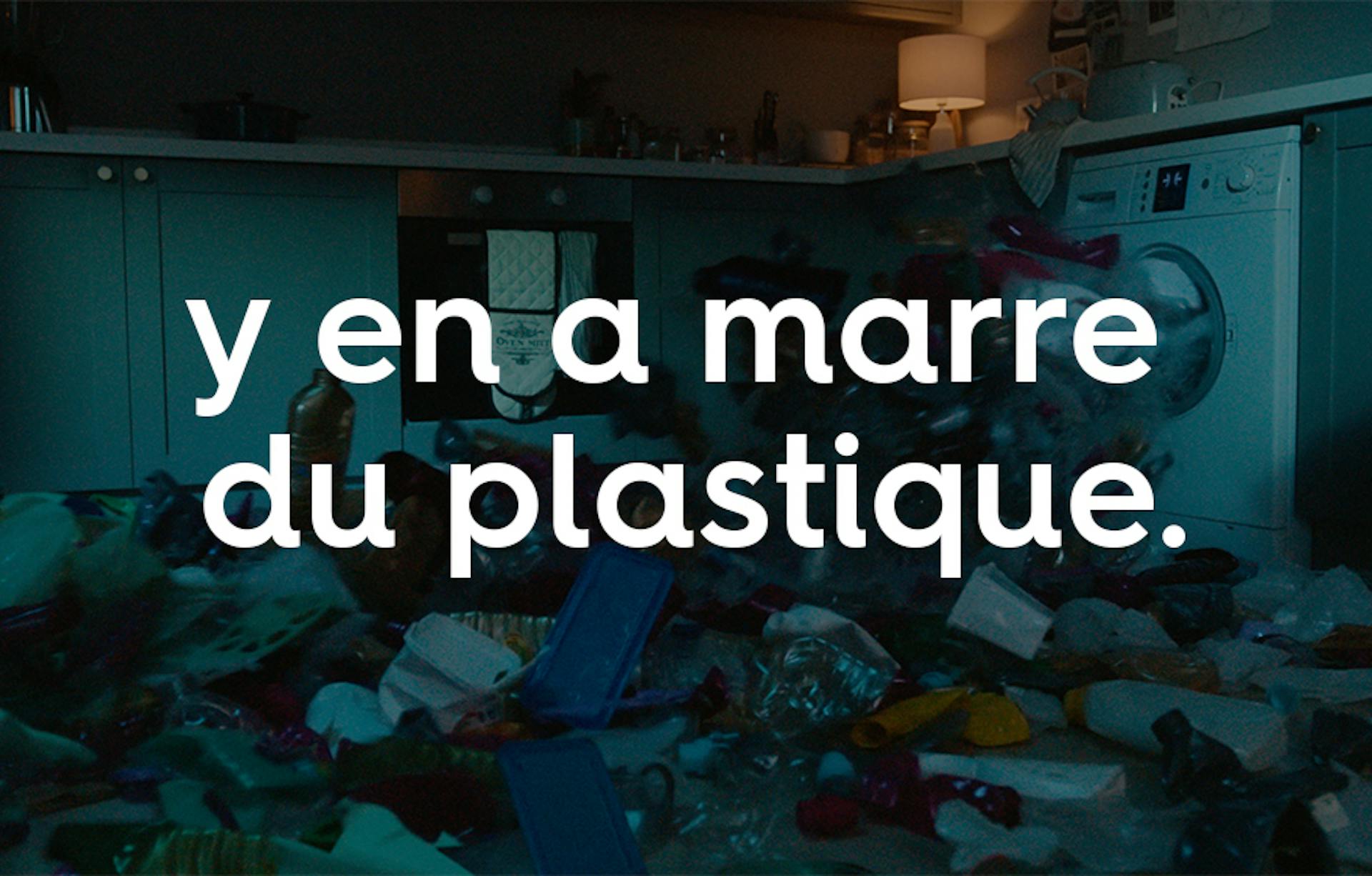 déchets en plastique sortant d’une machine à laver derrière le texte « y en a marre du plastique ».