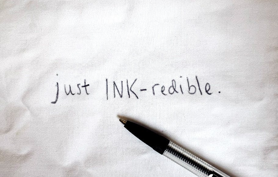 biro written on white fabric. text: just ink-redible