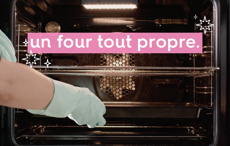 un four ouvert avec la lumière allumée et une main portant des gants en caoutchouc retirant la plaque du four pour la nettoyer.