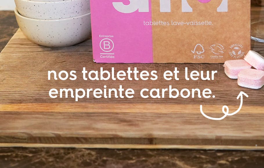 le texte « nos tablettes et leur empreinte carbone » en police d'écriture blanche devant un pack de tablettes lave-vaisselle, trois tablettes et deux bols blancs le tout sur une table en bois.