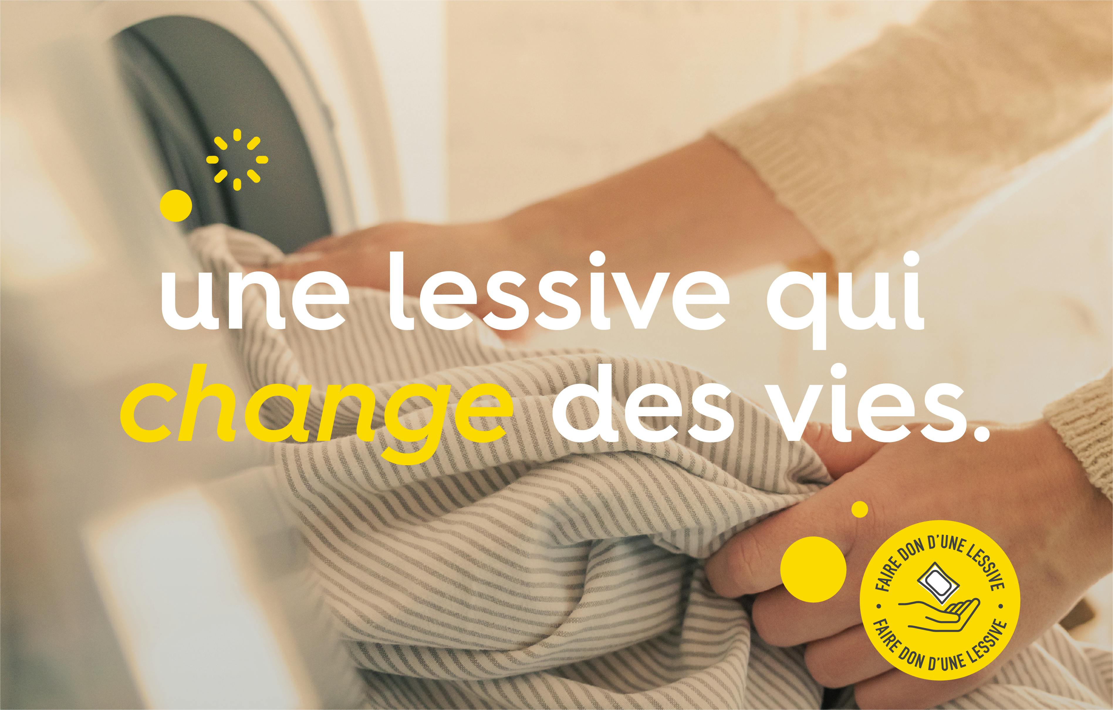 une paire de main sortant un vêtement d'une machine à laver avec le texte « une lessive qui change des vies »