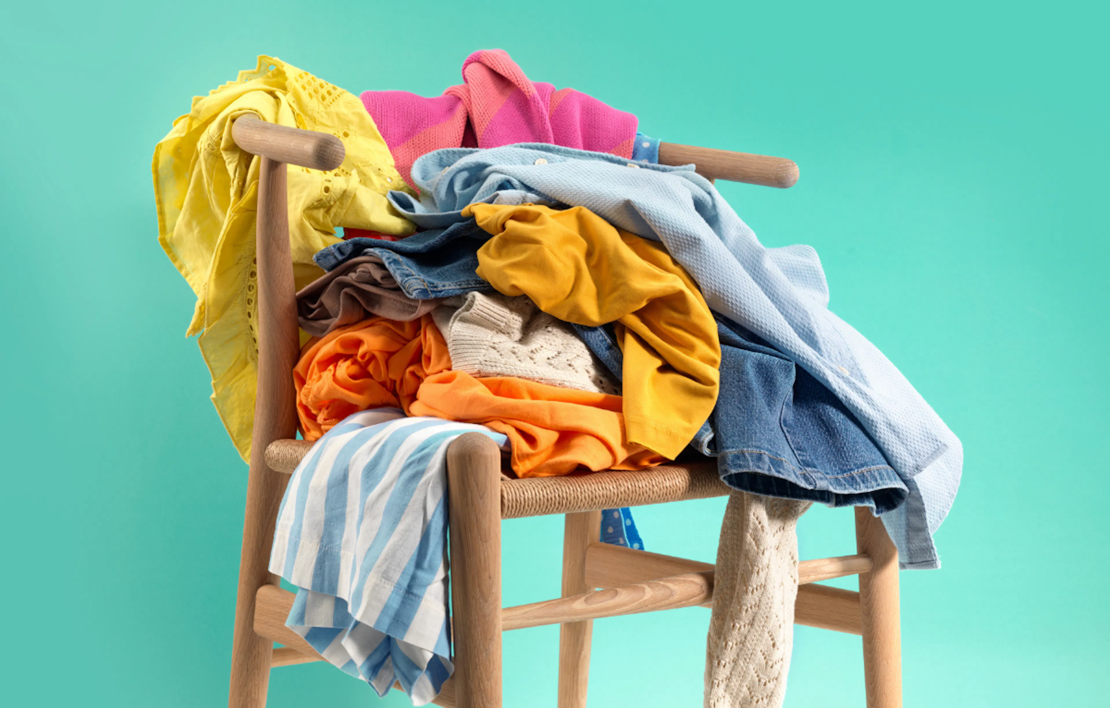 a wooden chair full of colourful clothing against a green blue background