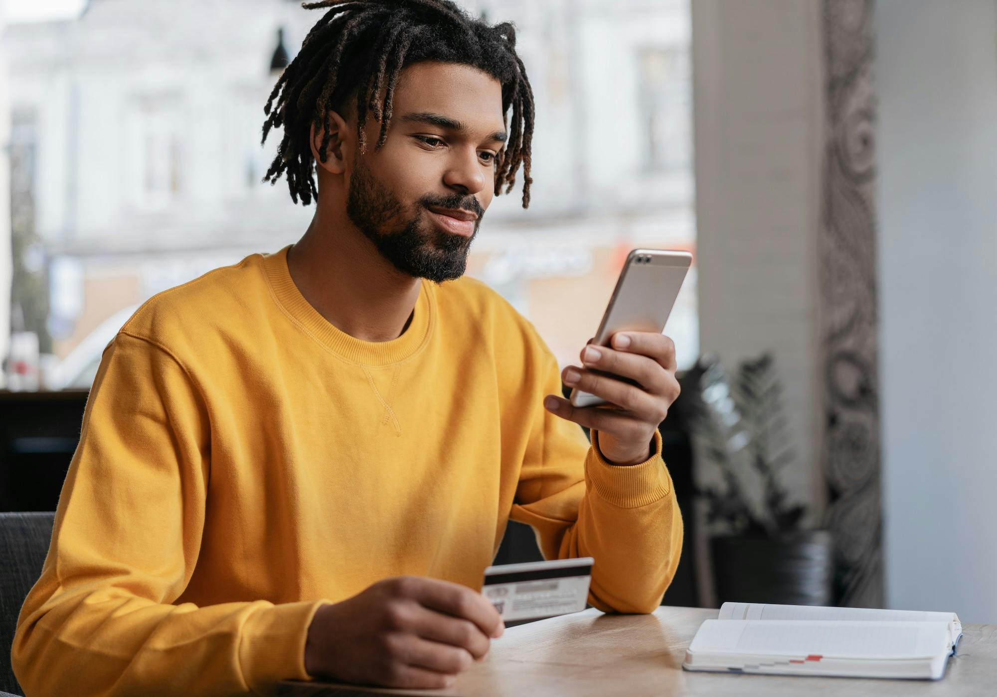 African American man holding credit card, using smartphone for online shopping, mobile banking. Young freelancer receive payment, check balance. Pensive hipster ordering food online, booking tickets.