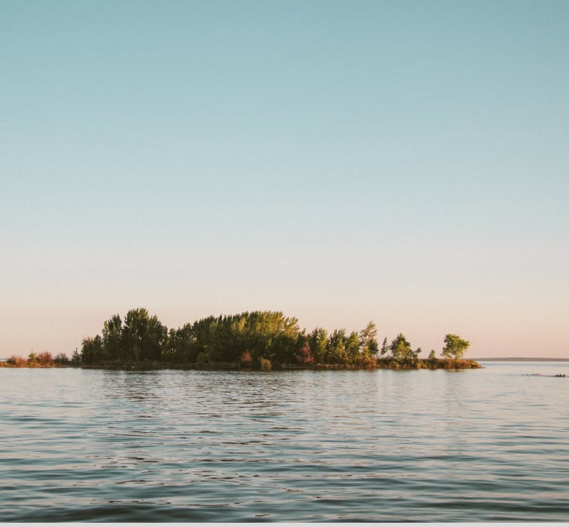 Photo of a body of water with an island in the middle that has trees