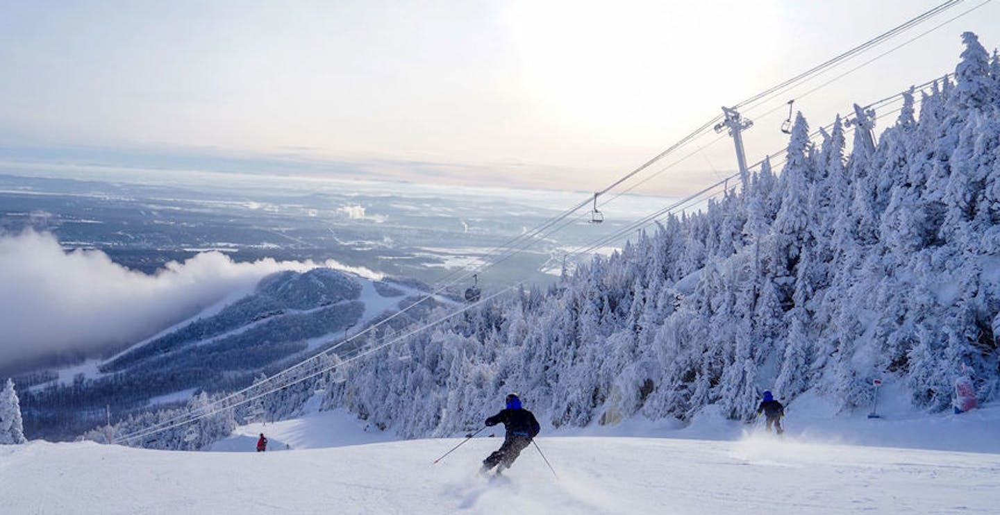 Two skiers in matching blue and black ski attire hitting wide open groomers at Mont Orford in Quebec, Canada, near Montreal.