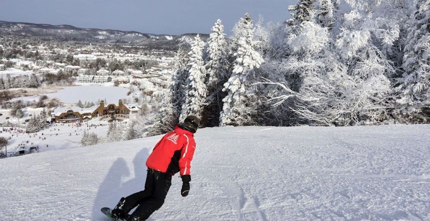 Male skier in red ski jacket and black ski pants hitting the slopes at Sommet Saint-Sauveur in Quebec, Canada, near Montreal.