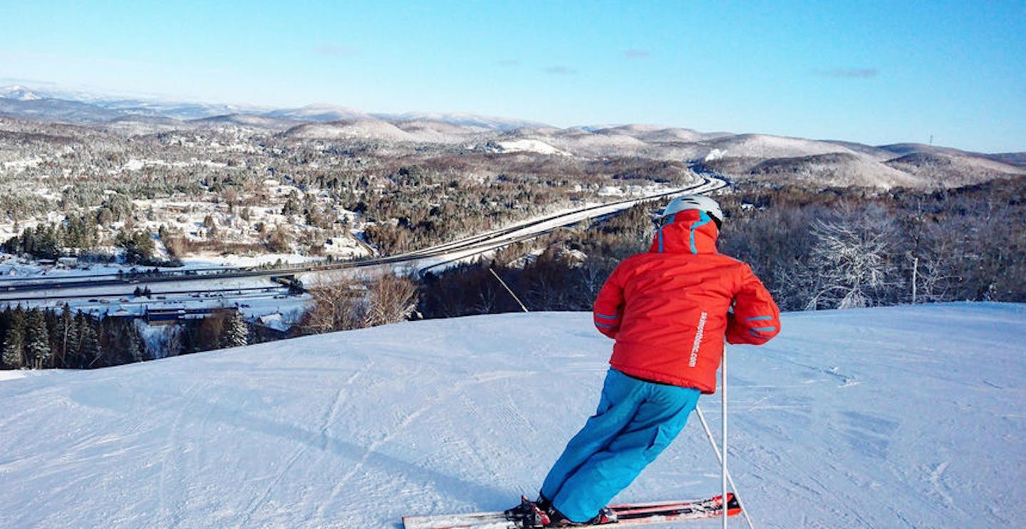 Skier of undiscernible gender in orange ski jacket and blue ski pants hitting the slopes at Mont Blanc in Quebec, Canada, near Montreal.