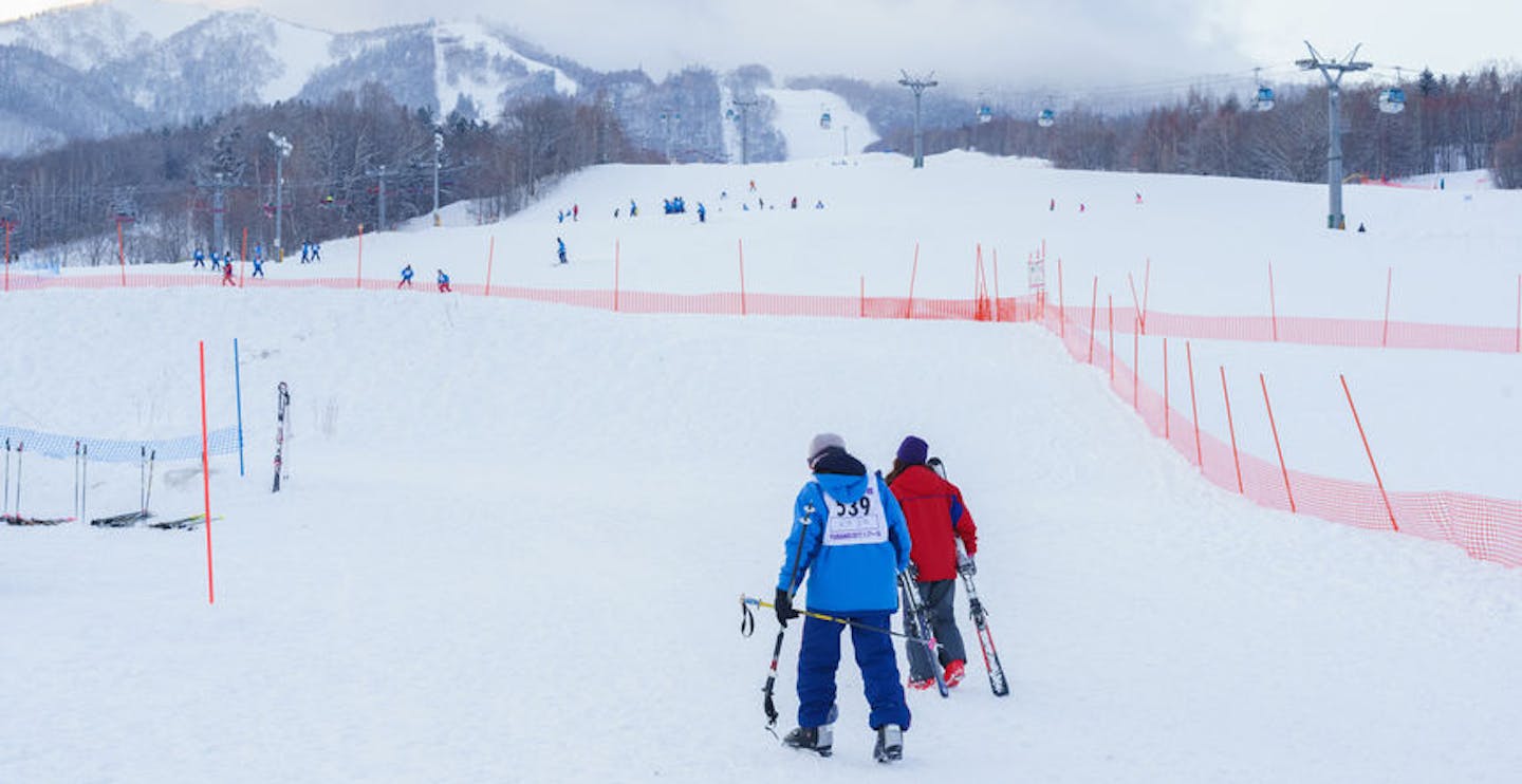 Two skiers in colorful ski attire walking up the slopes at Furano Ski Resort in Hokkaido, Japan.