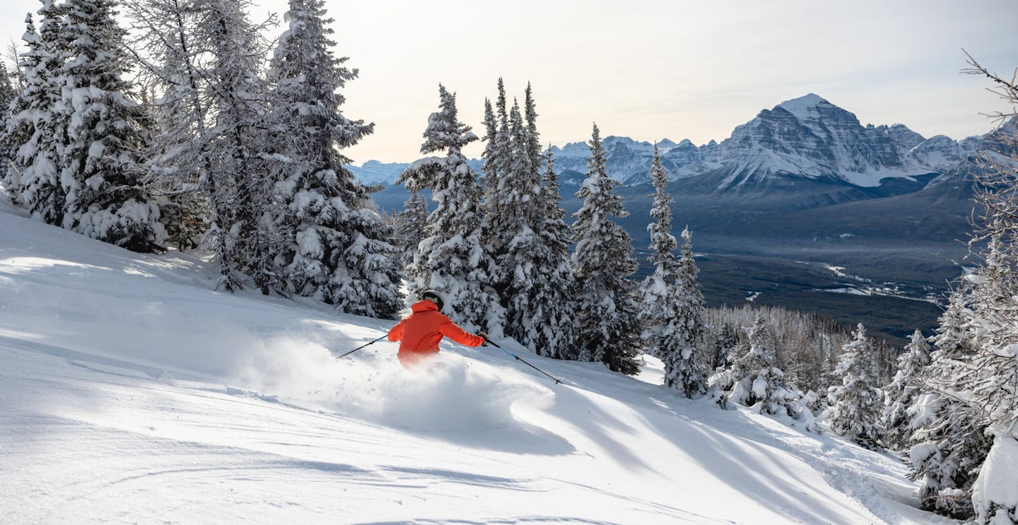 Skier of undiscernible gender in orange ski jacket hitting the slopes at Lake Louise in Alberta, Canada.