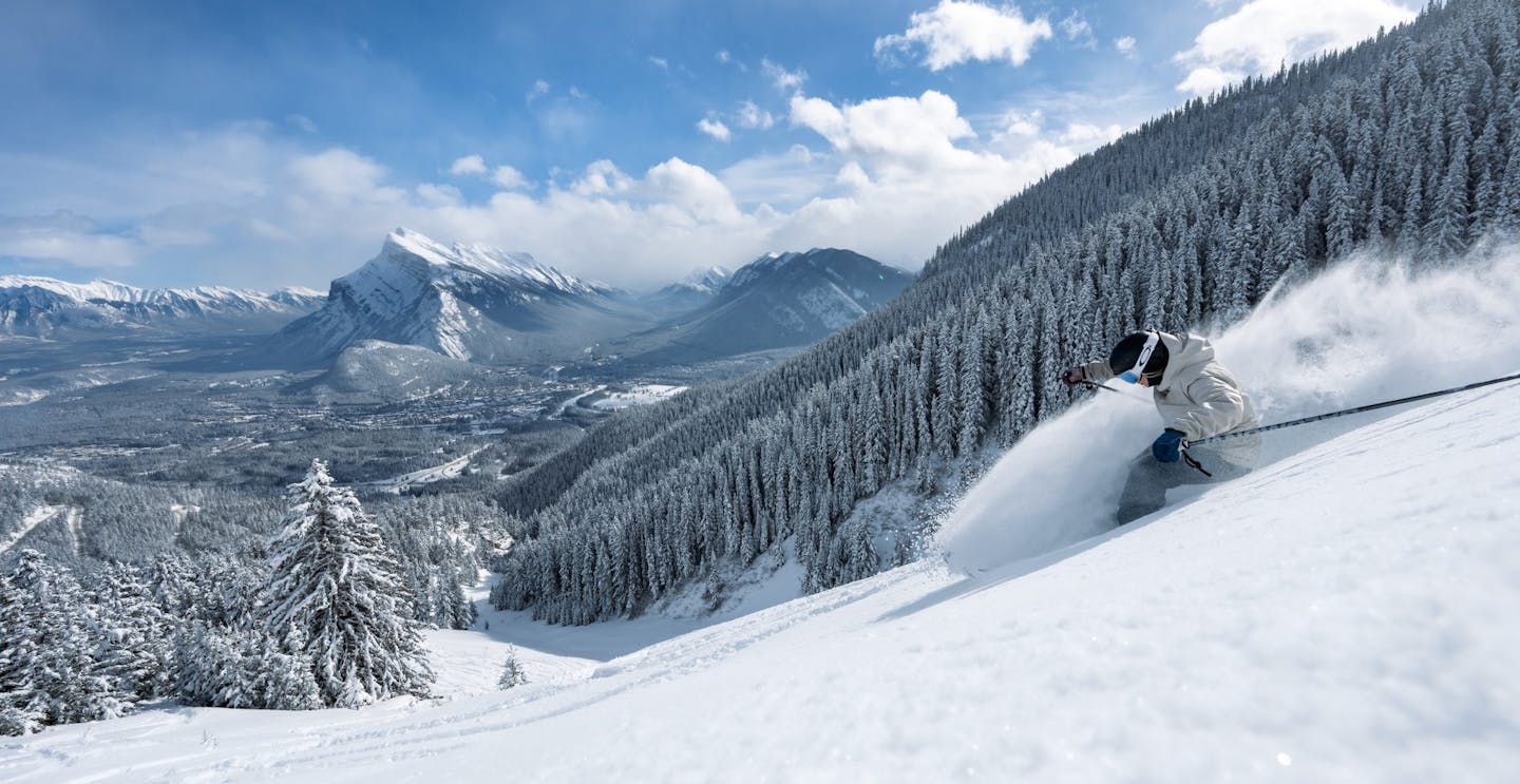 Skier of undiscernible gender in white ski jacket hitting the frozen slopes at Mount Norquay in Alberta, Canada.