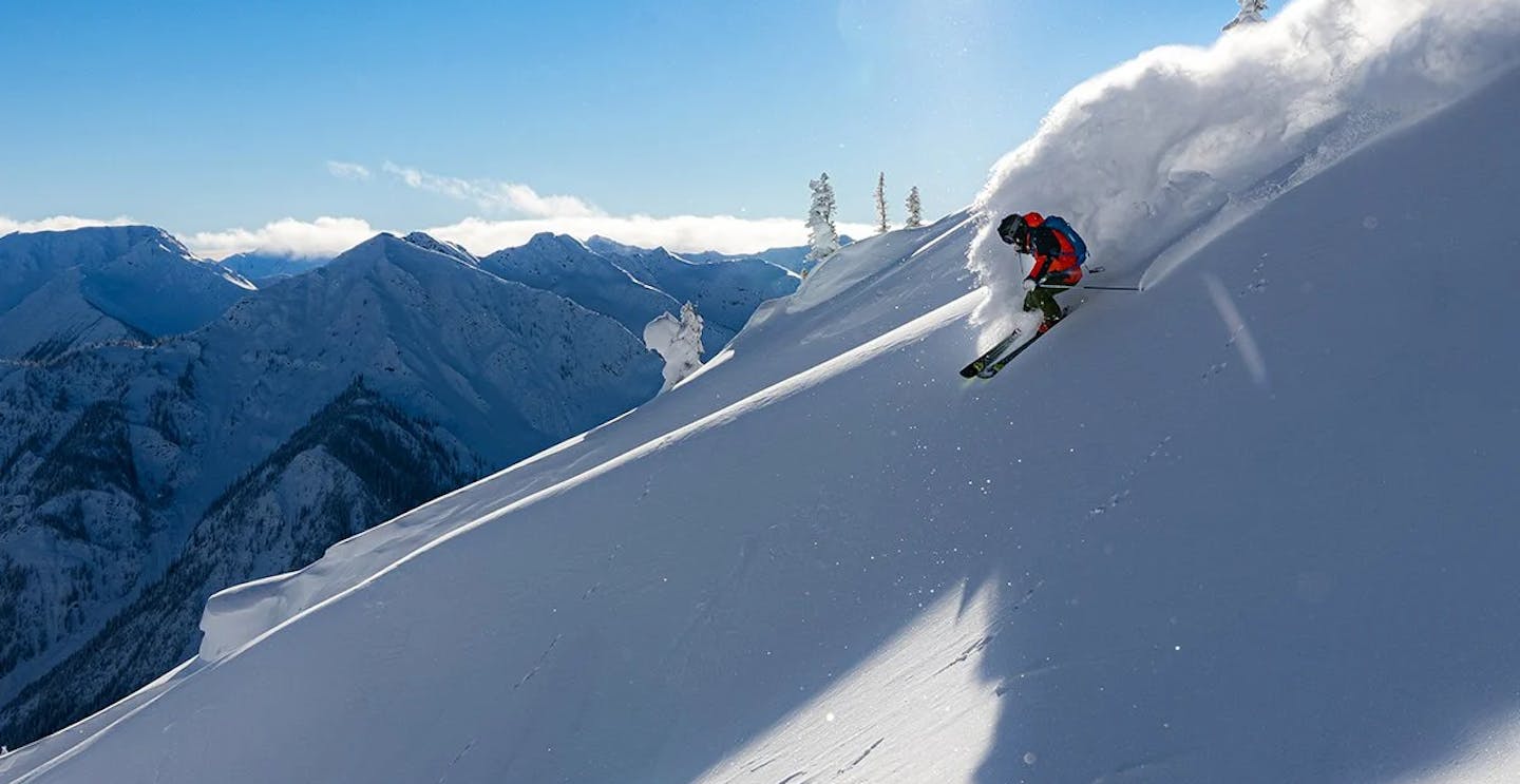 Skier of undiscerible gender in orange ski suit hitting the slopes at Fernie Alpine Resort in British Columbia, Canada.