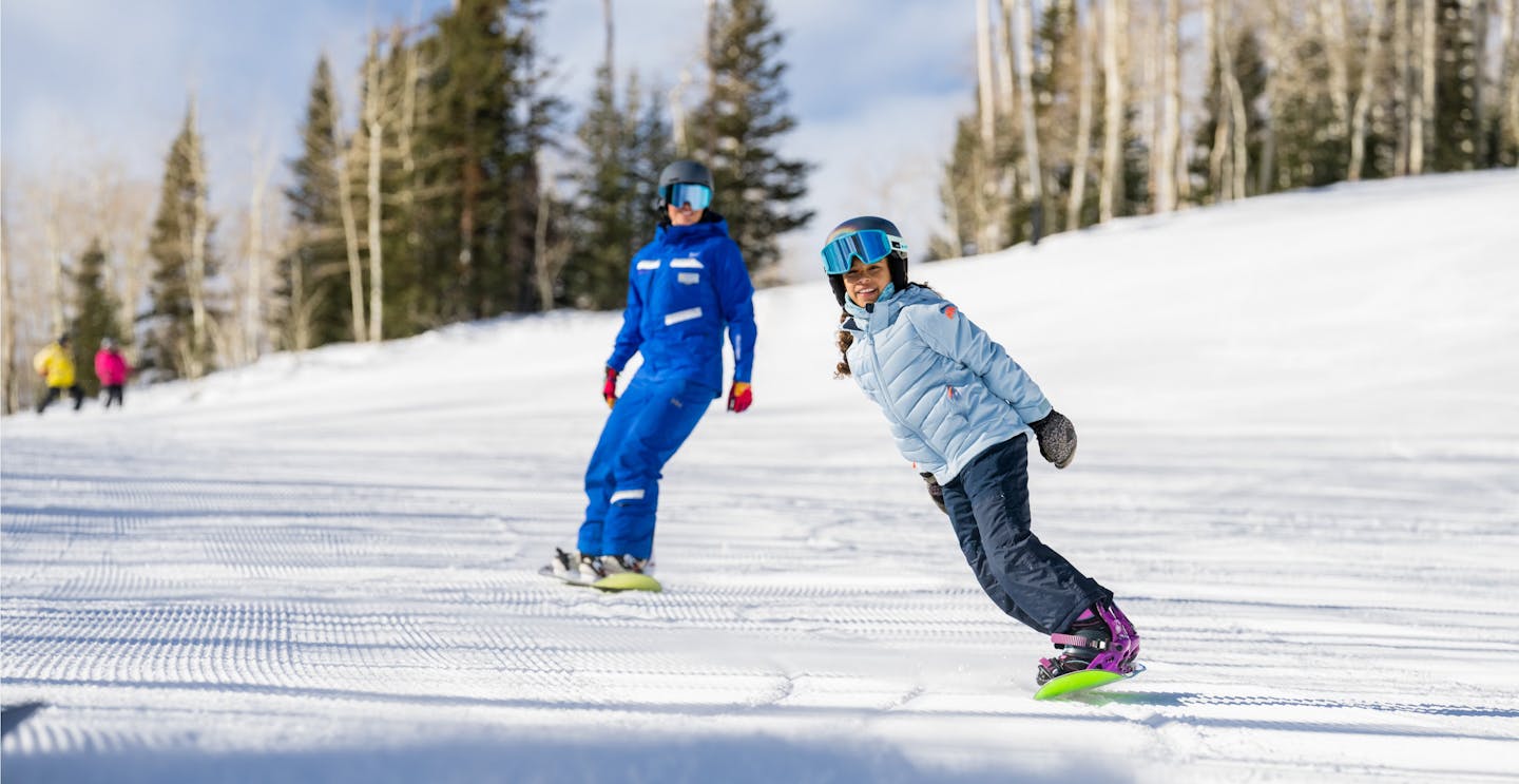 Female snowboard guide in blue snowboard gear and her young student in baby blue snowboard jacket hitting the slopes in Park City in Utah, USA, near Salt Lake City.