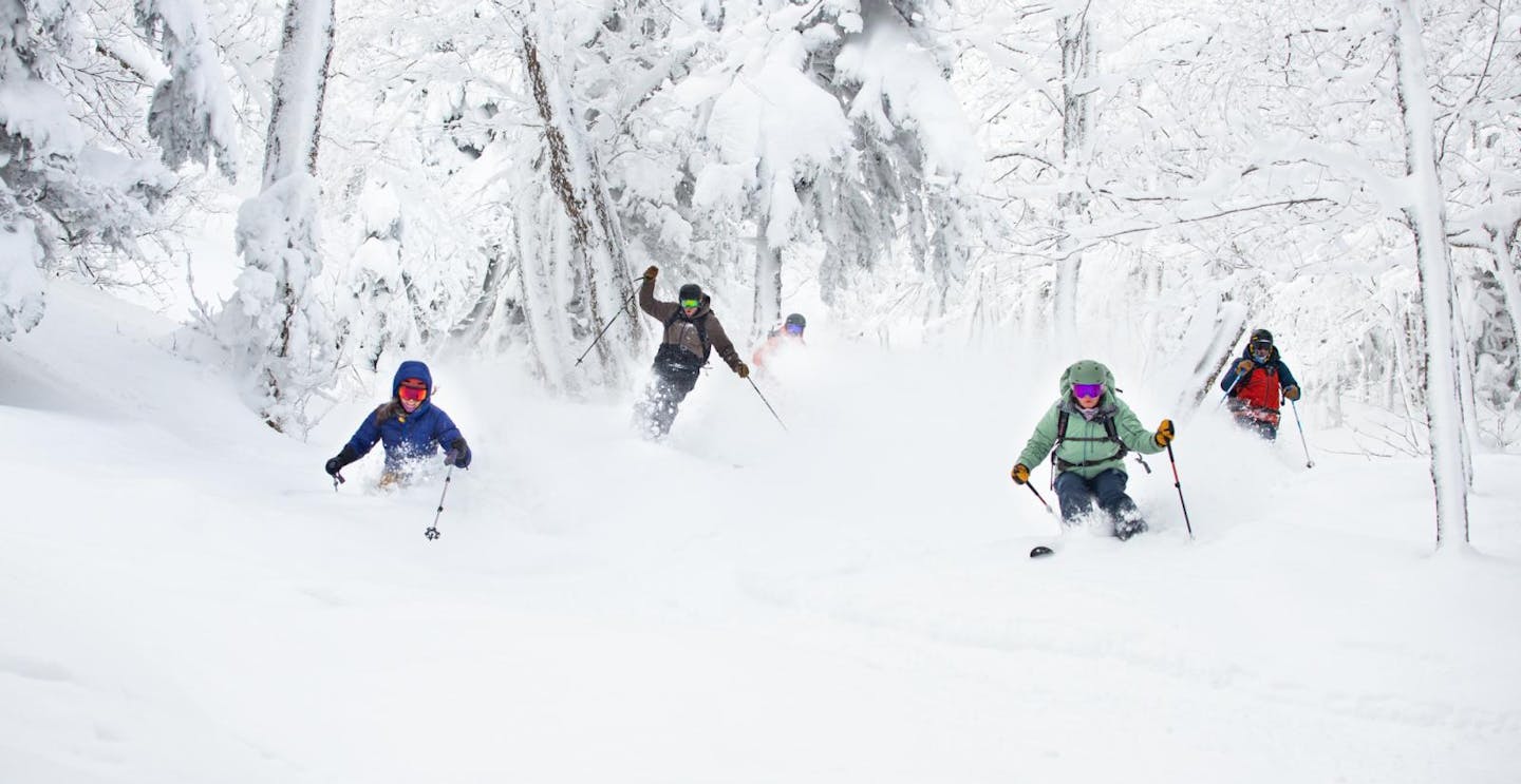 Four skiers of undiscernible gender hitting the slopes at Jay Peak on the East Coast of the United States.