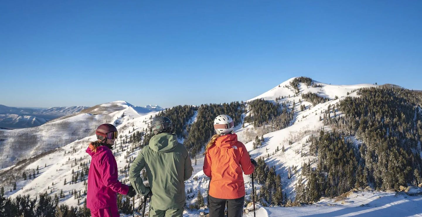 Three skiers in colorful ski attire taking in the views at Deer Valley Resort in Park City, Utah, USA, near Salt Lake City.