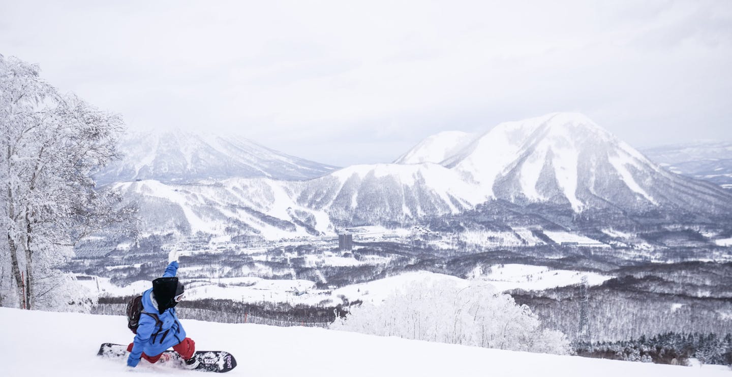 Skier of undiscernible gender in blue ski jacket and red ski pants hitting the slopes at Rusutsu in Japan.