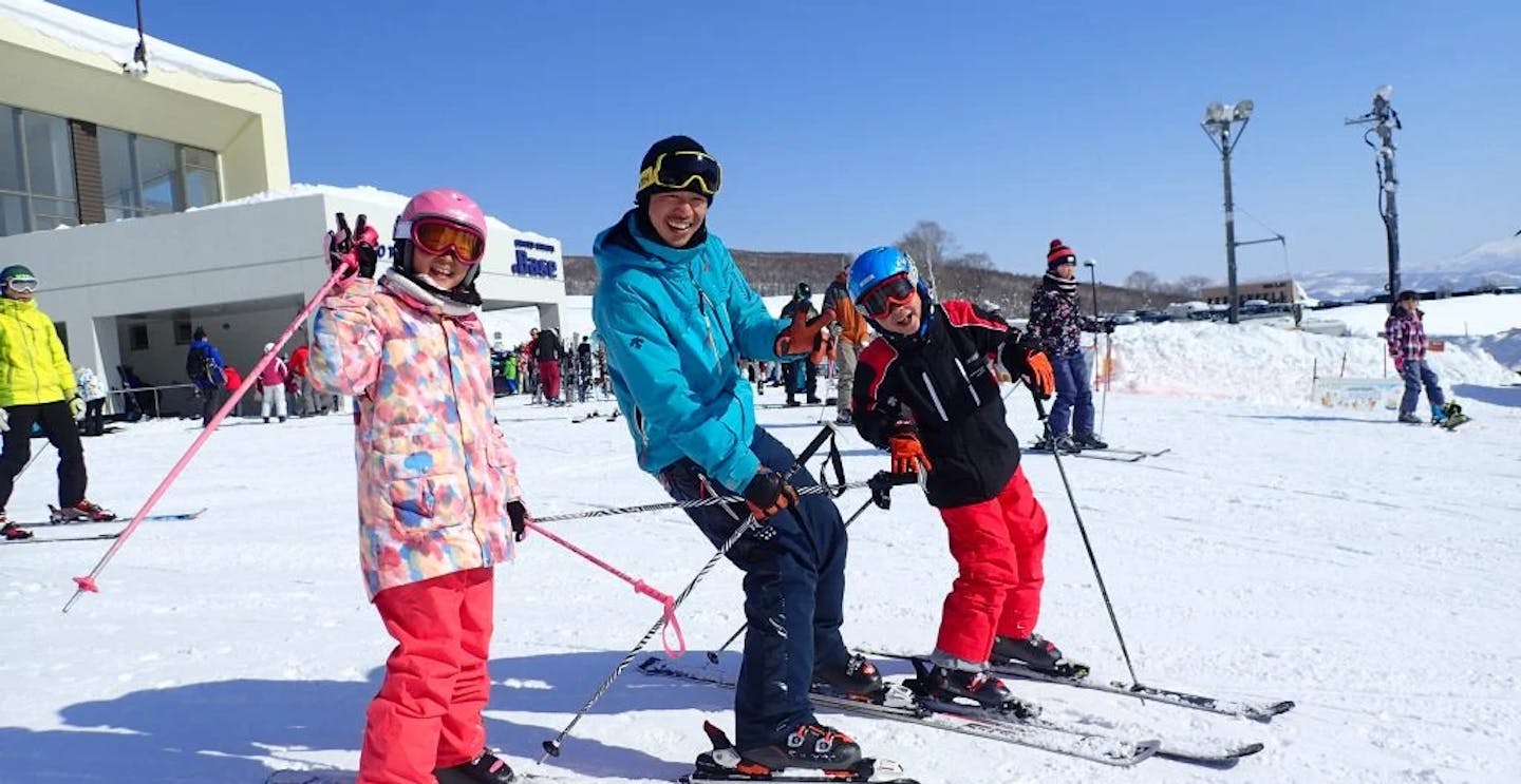 Male ski guide in blue ski jacket with two child skiers in colorful ski attire taking a photo at Niseko in Hokkaido, Japan.