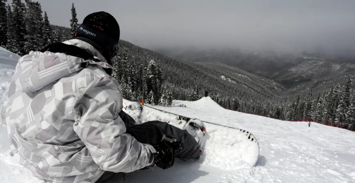 Male snowboarder in black and white snowboarder attire on a misty day sitting on the slopes of Echo Mountain in Colorado, USA, near Denver.