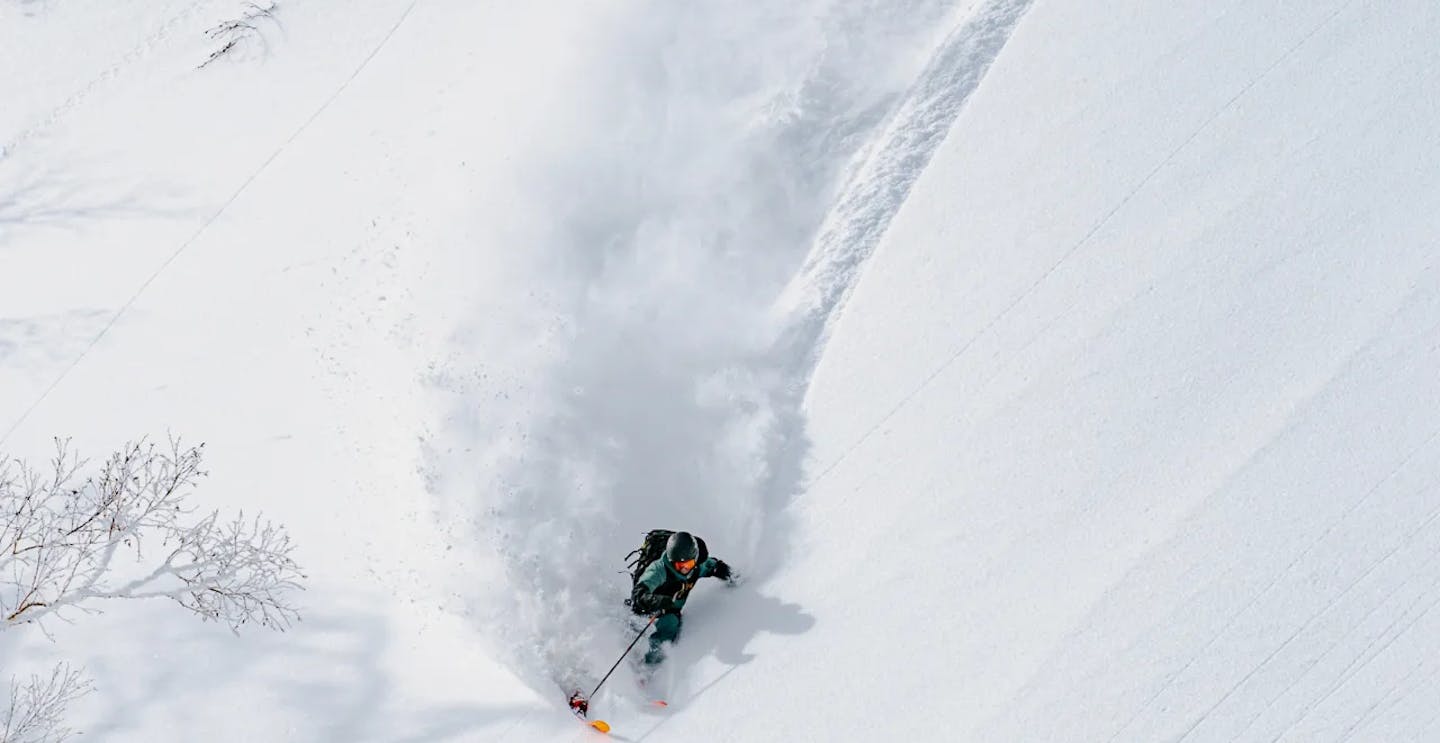 Skier of undiscernible gender in dark teal and black ski attire hitting the slopes at Sapporo Teine in Japan.