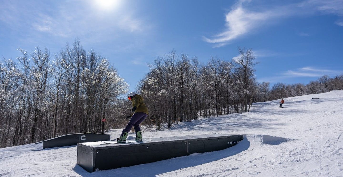 Snowboarder of undiscernible gender in green snowboarding jacket hitting the terrain park at Mount Snow in Vermont, USA.