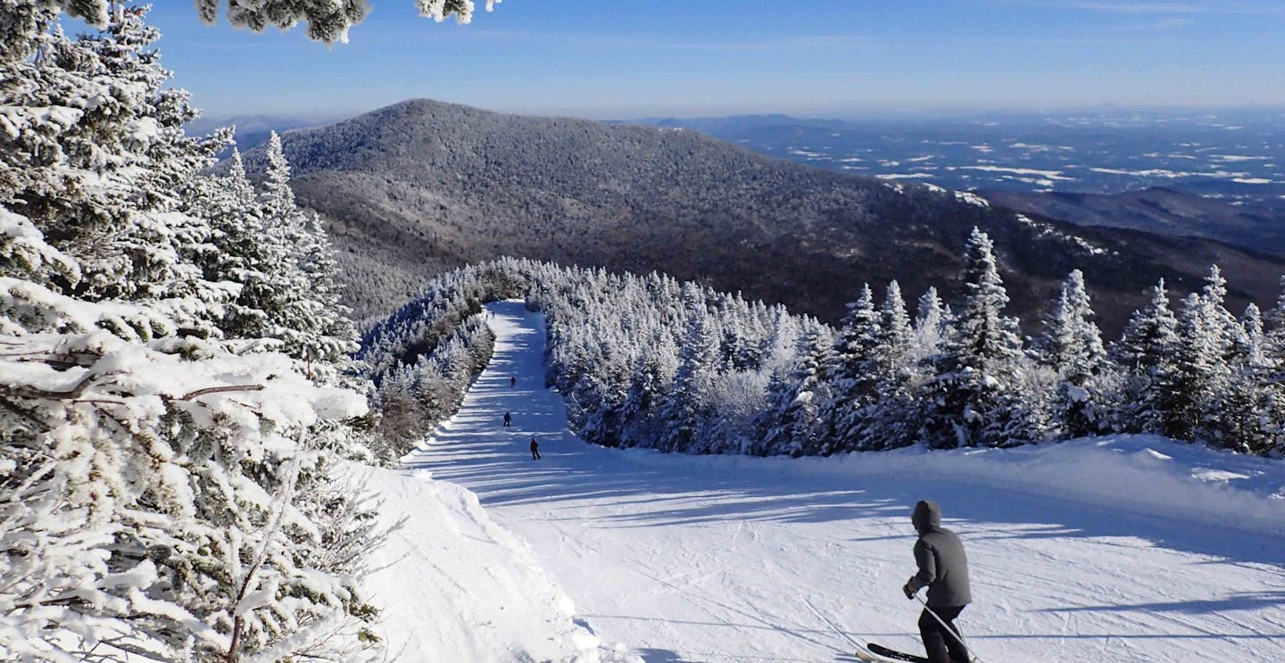 Skier of undiscernible gender in grey ski jacket hitting the slopes at Smugglers' Notch Resort in Vermont, USA.