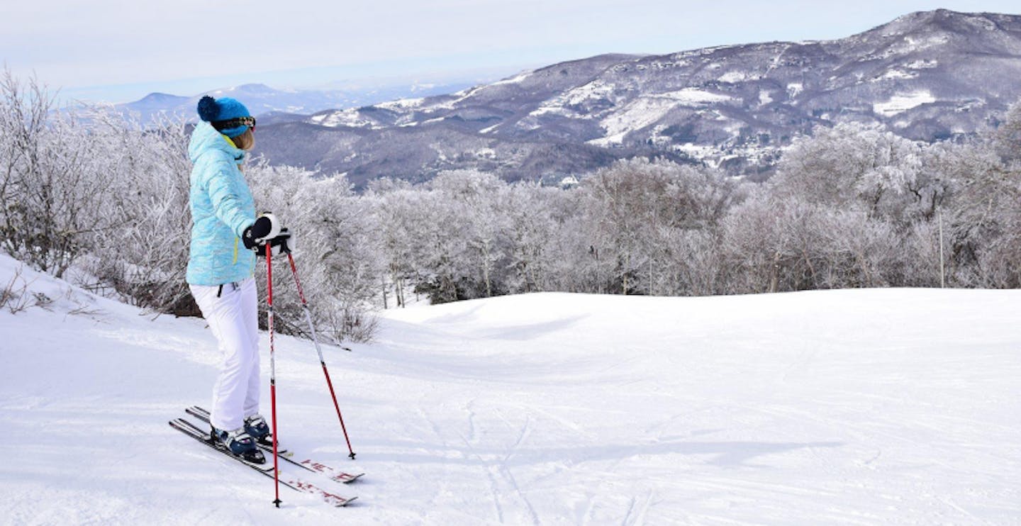 Female skier in baby blue ski jacket and white ski pants taking in the views at Sugar Mountain Resort in North Carolina, USA.