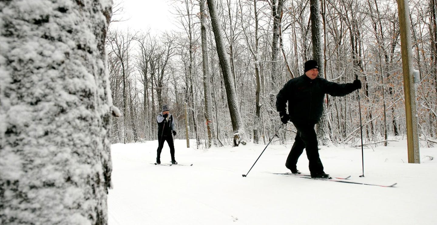 Two male skiers in black ski attire partaking in Nordic skiing at Bristol Mountain in New York, USA. 