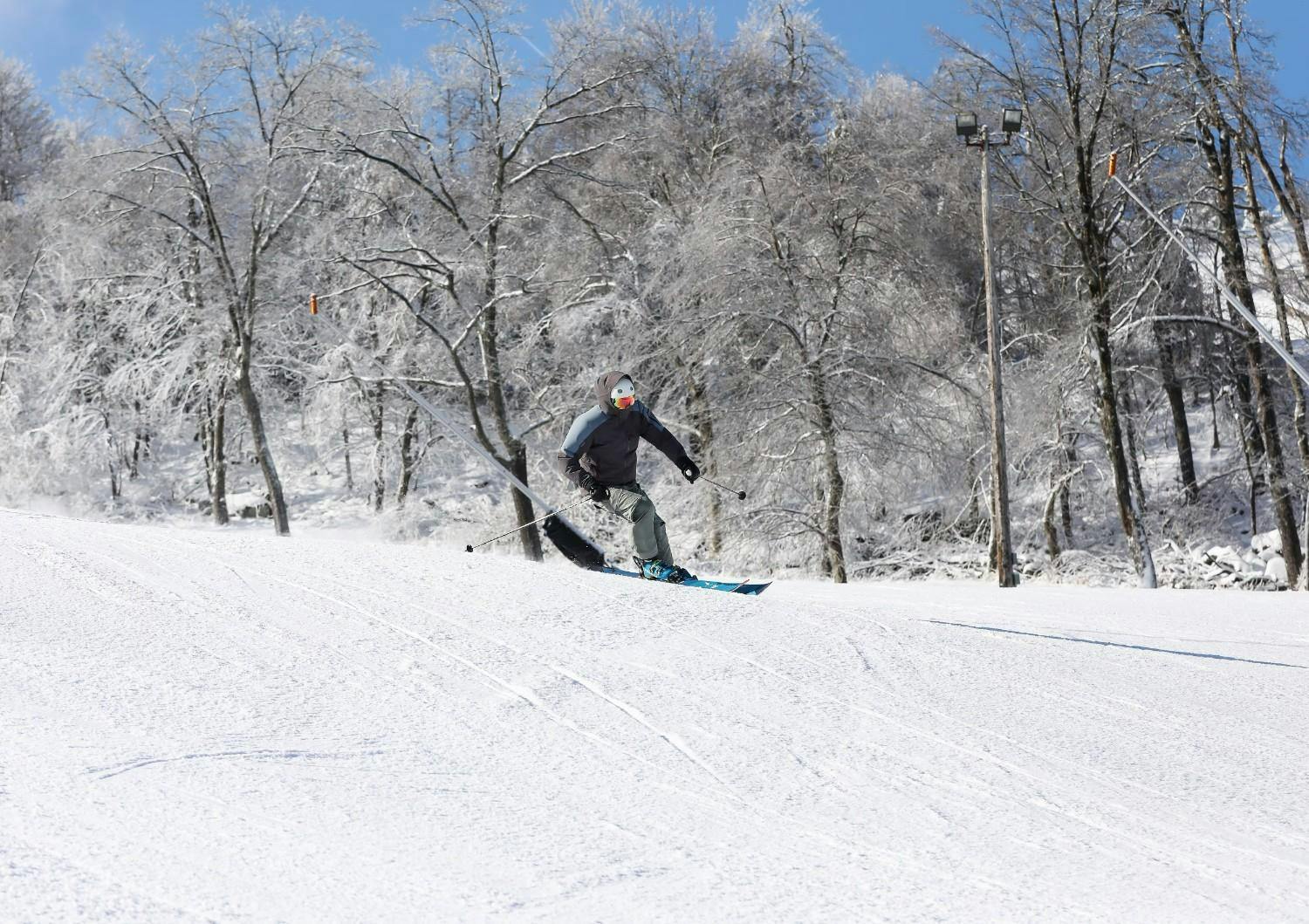 Skier of undiscernible gender in dark-colored ski attire hitting the slopes at Seven Springs Mountain Resort in Pennsylvania, USA.