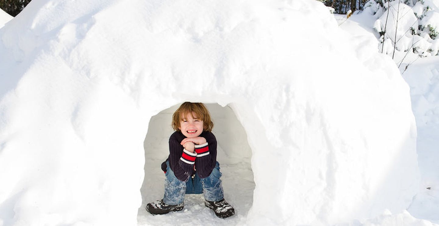 Funny boy playing in a snow igloo