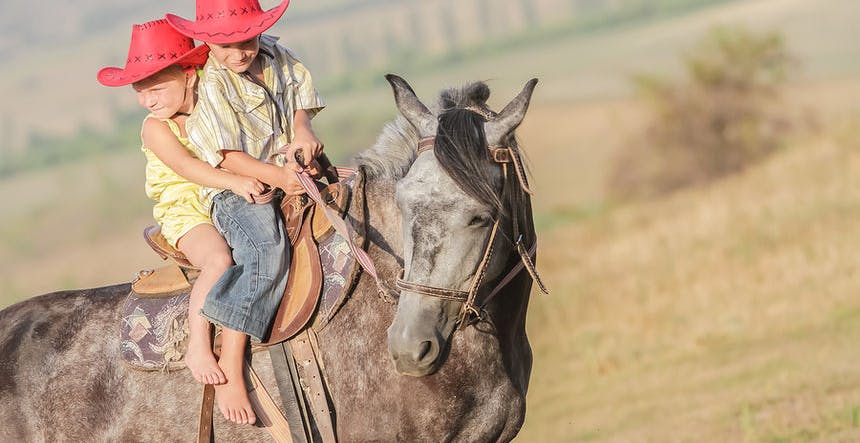 Two young happy kids riding a horse