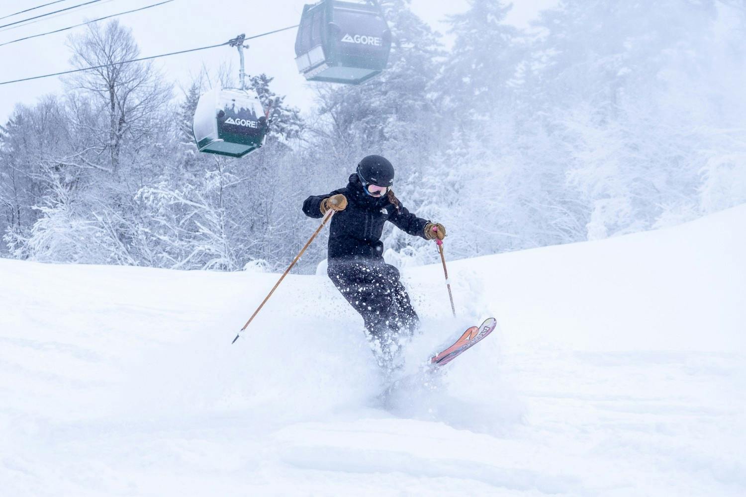 Skier of undiscernible gender in black ski attire hitting the slopes with the gondola running in the backdrop at Gore Mountain in New York, USA.
