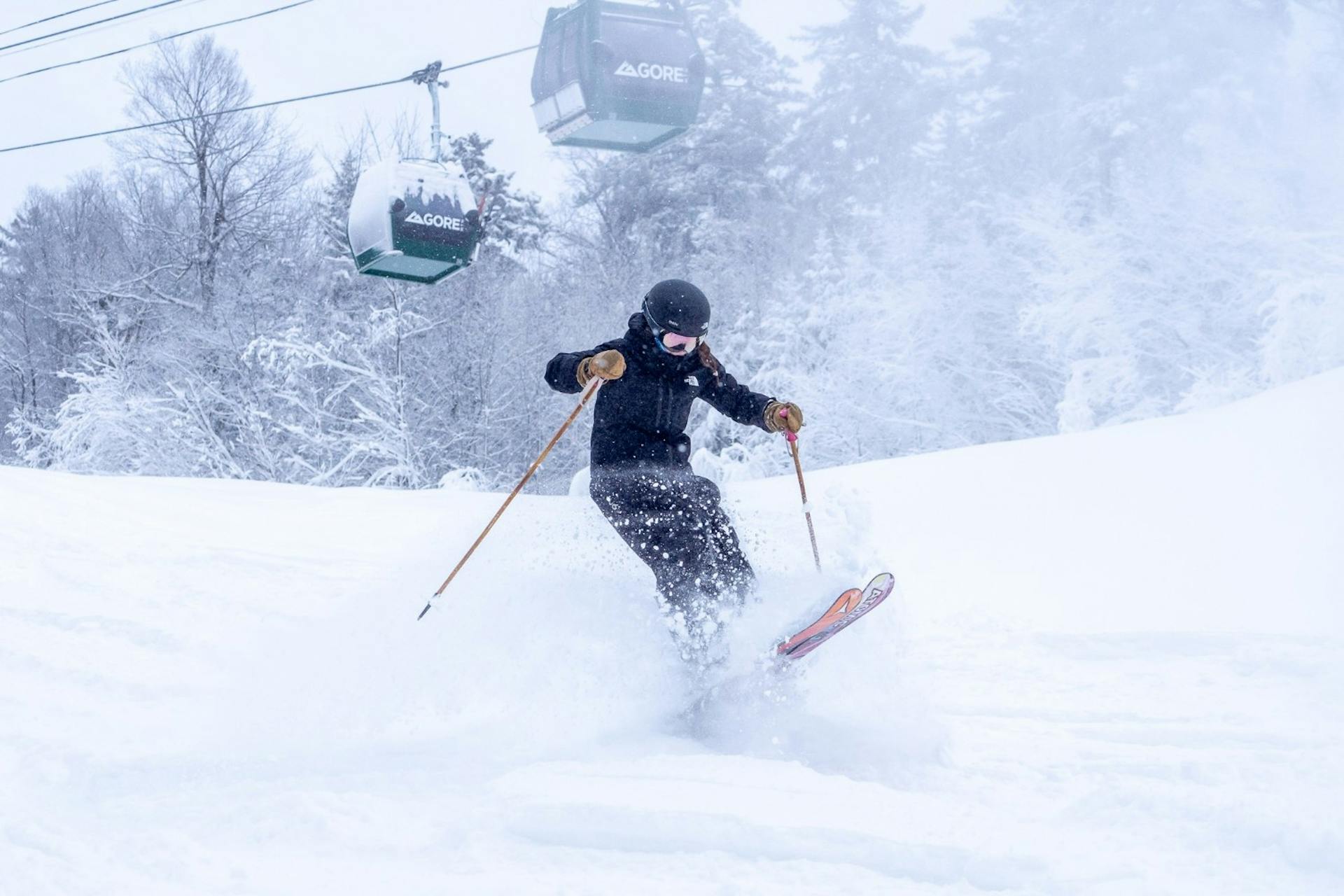 Skier of undiscernible gender in black ski attire hitting the slopes with the gondola running in the backdrop at Gore Mountain in New York, USA.