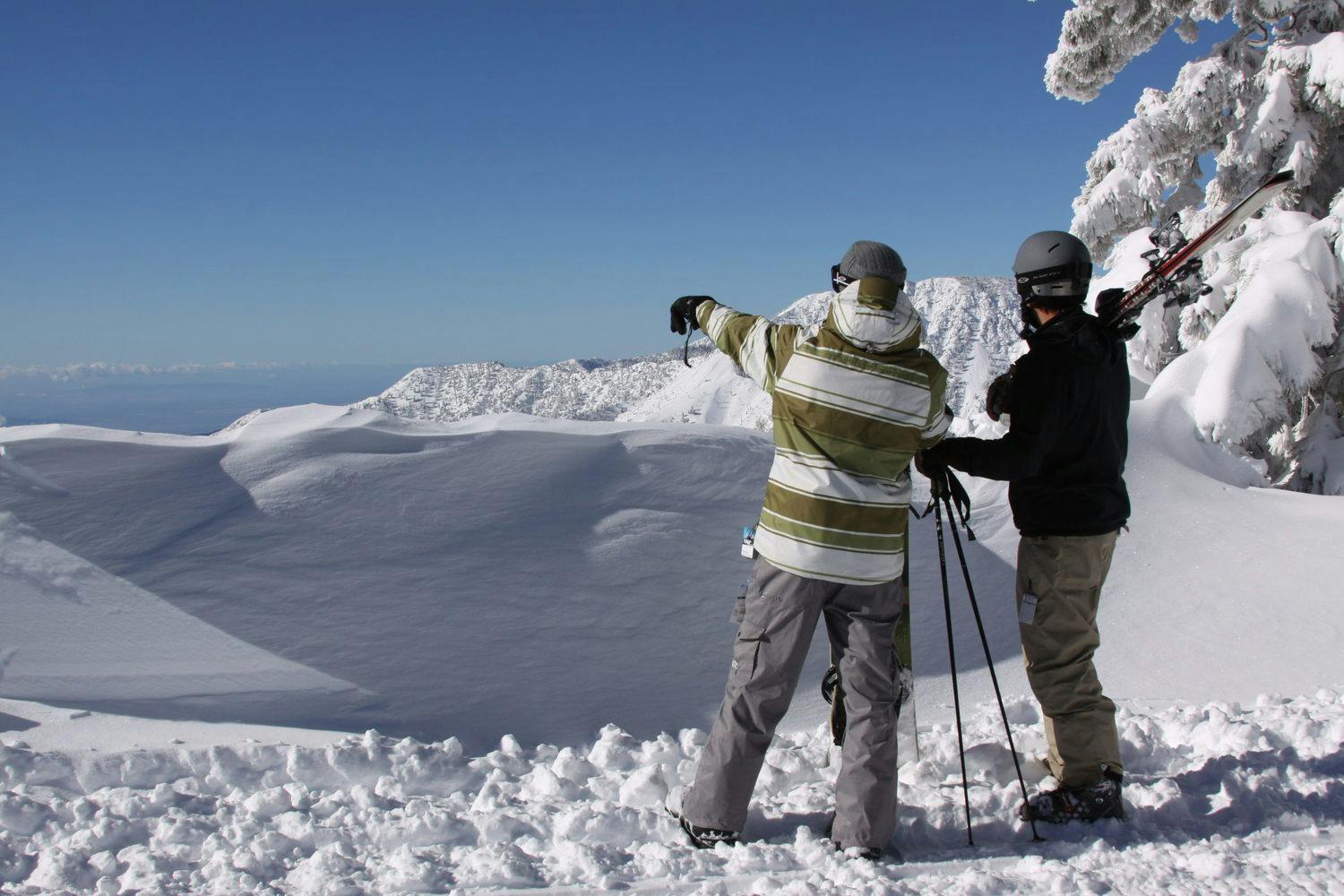 Two male skiers in muted-toned ski attire taking in the views on the summit of Mountain High near Los Angeles in California, USA.