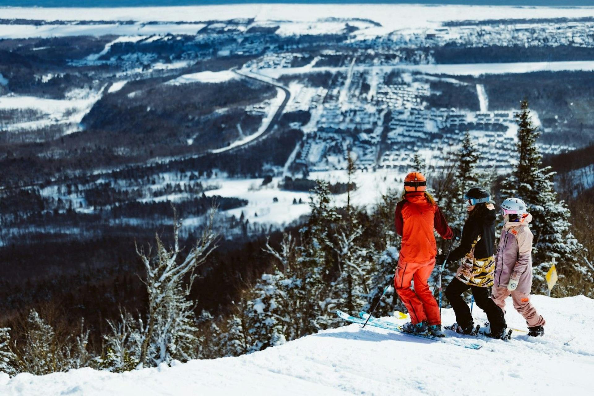 Three diverse young skiers in colorful ski attire checking out the views at Mont-Sainte-Anne near Montreal in Quebec, Canada.