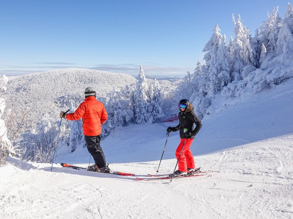 Two skiers in bright orange and black ski attire hitting the slopes at Mont Sutton near Montreal in Quebec, Canada.