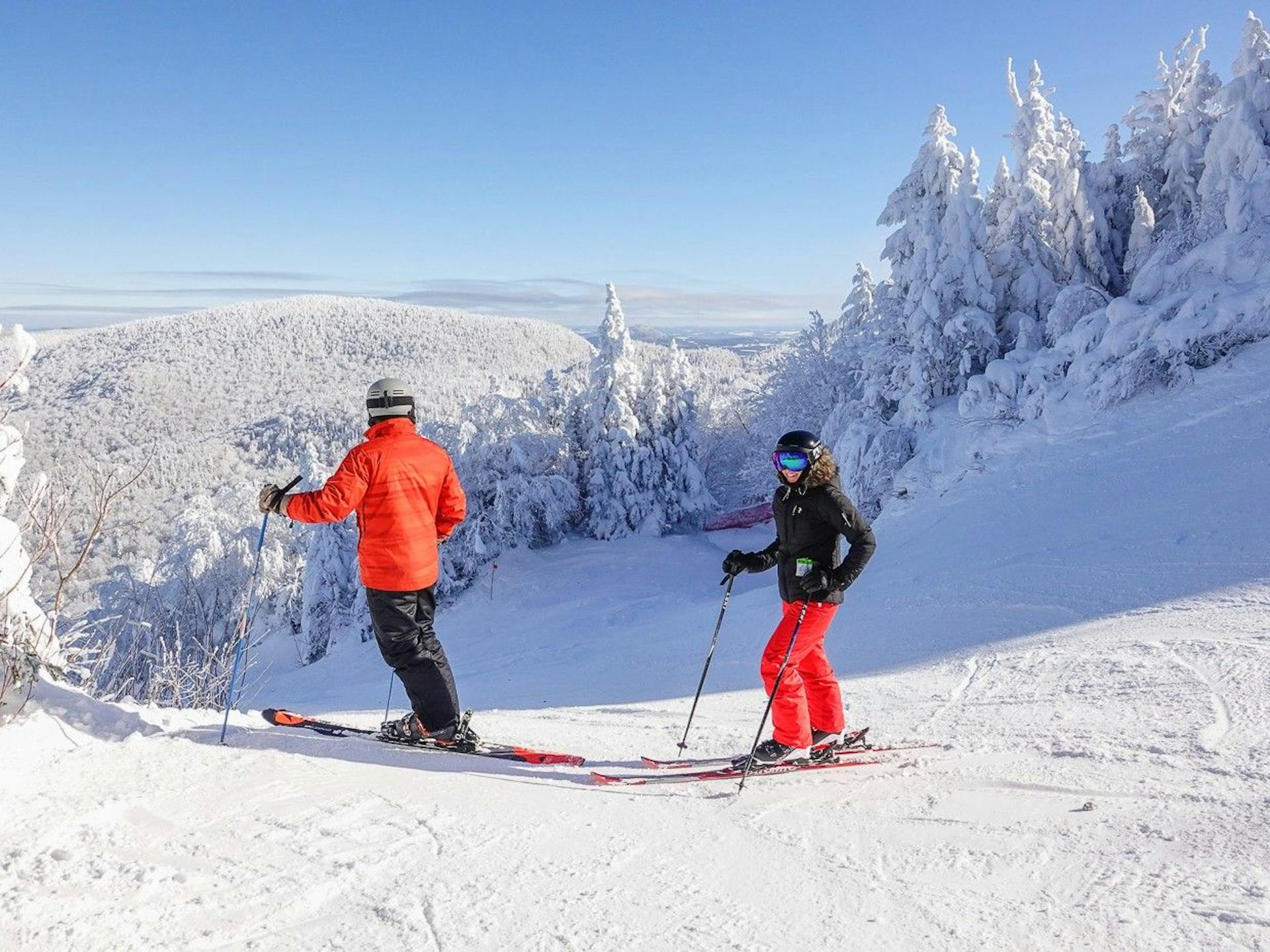 Two skiers in bright orange and black ski attire hitting the slopes at Mont Sutton near Montreal in Quebec, Canada.