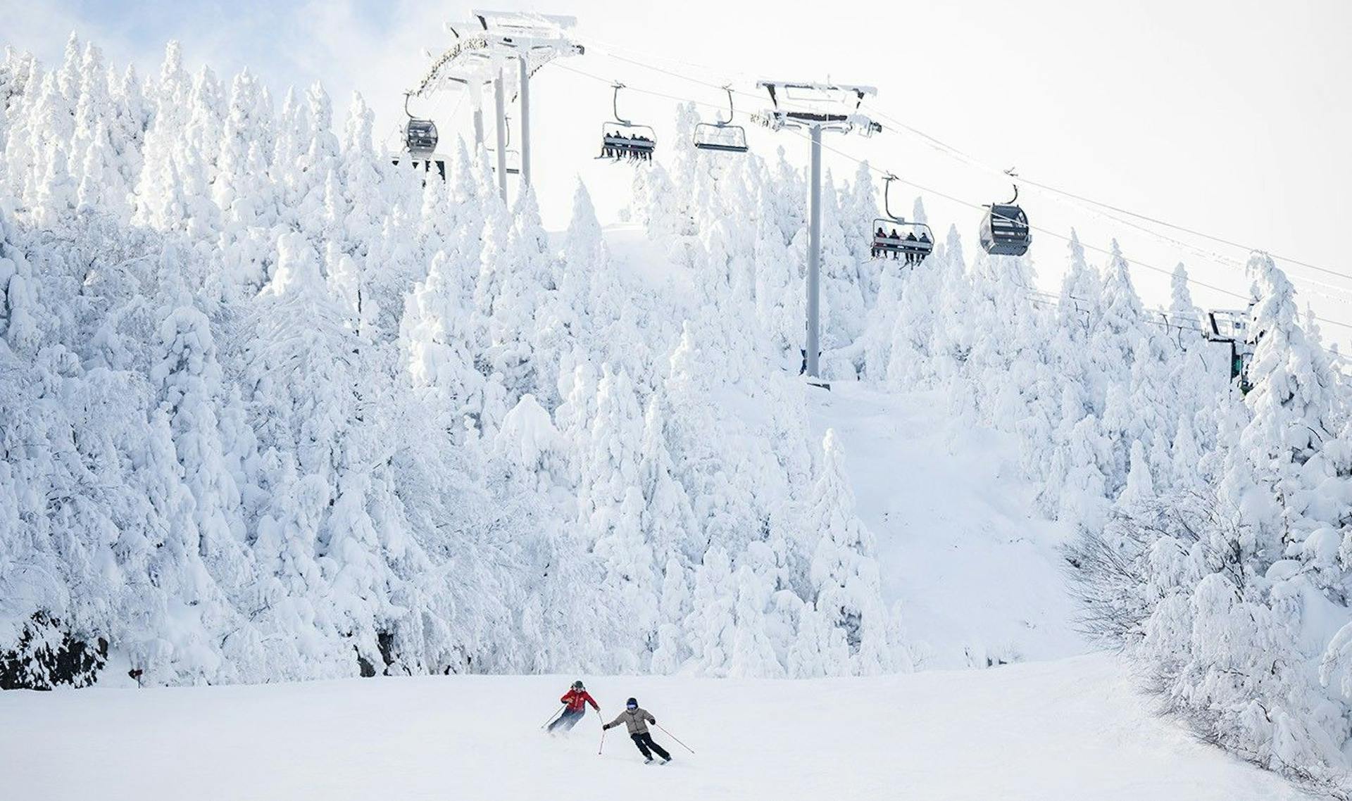 Two skiers of undiscernible gender in colorful ski attire hitting wide open groomers at Mont Orford near Montreal in Quebec, Canada.