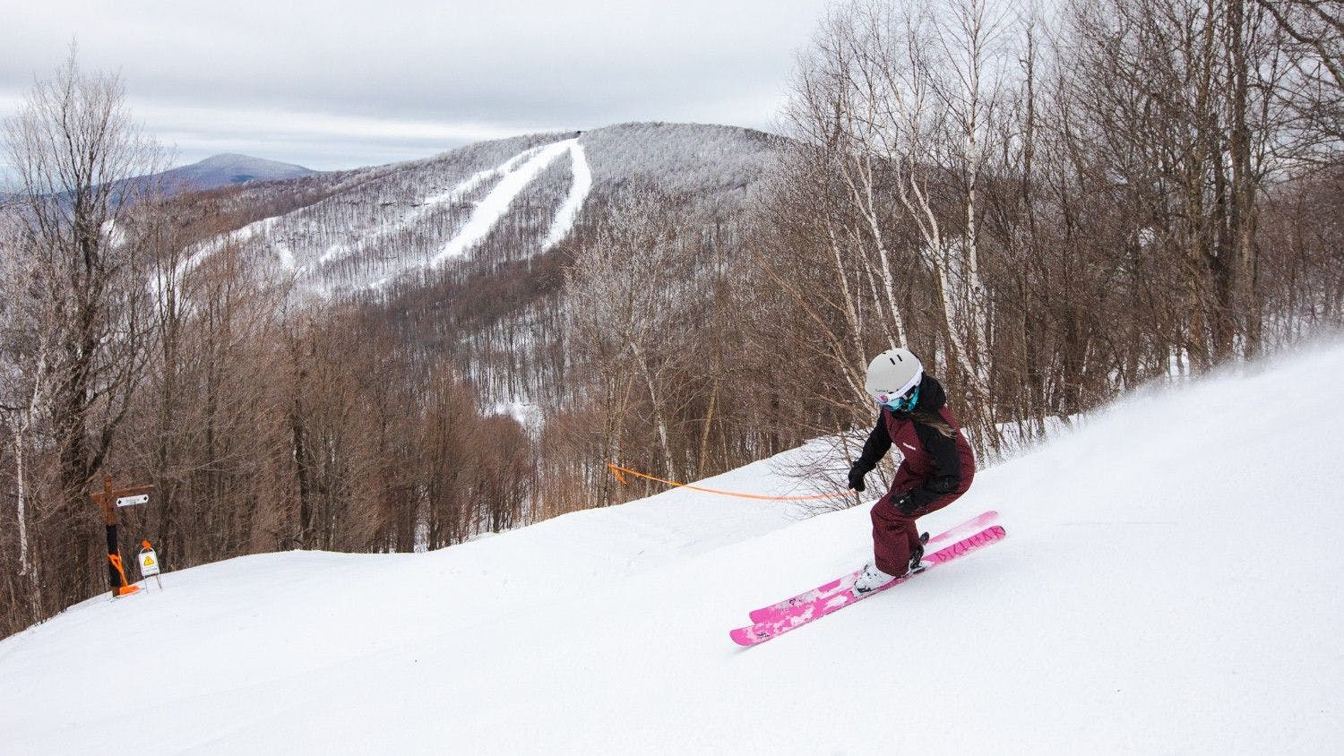 Female skier in black-and-maroon-colored ski attire and pink skis hitting the slopes at Windham Mountain in New York, USA.
