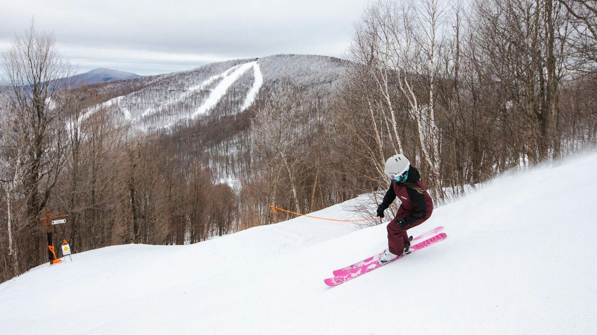 Female skier in black-and-maroon-colored ski attire and pink skis hitting the slopes at Windham Mountain in New York, USA.