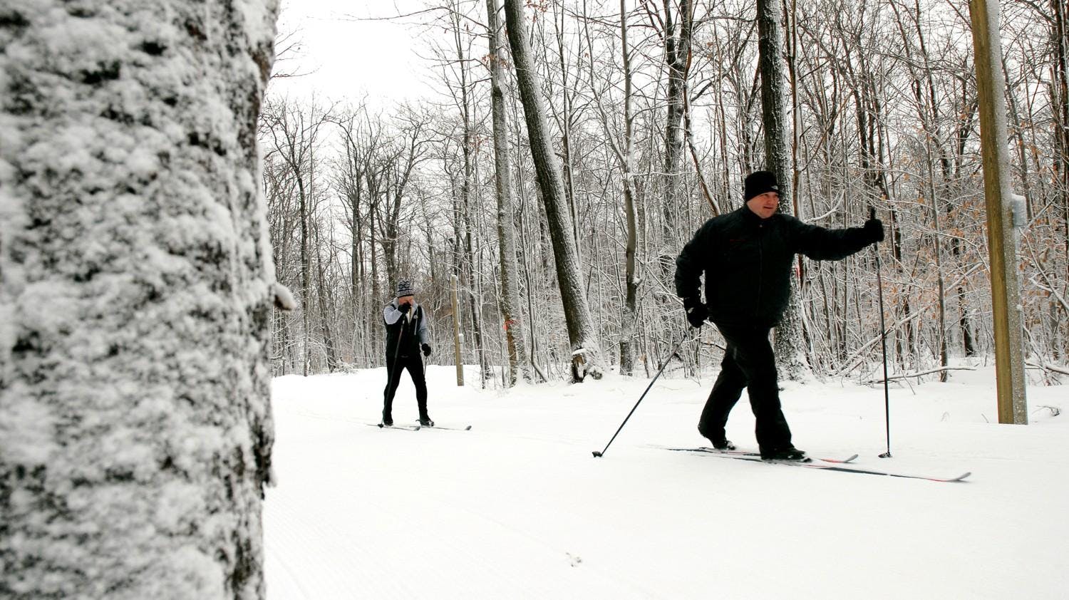 Two male skiers in black ski attire partaking in Nordic skiing at Bristol Mountain in New York, USA.