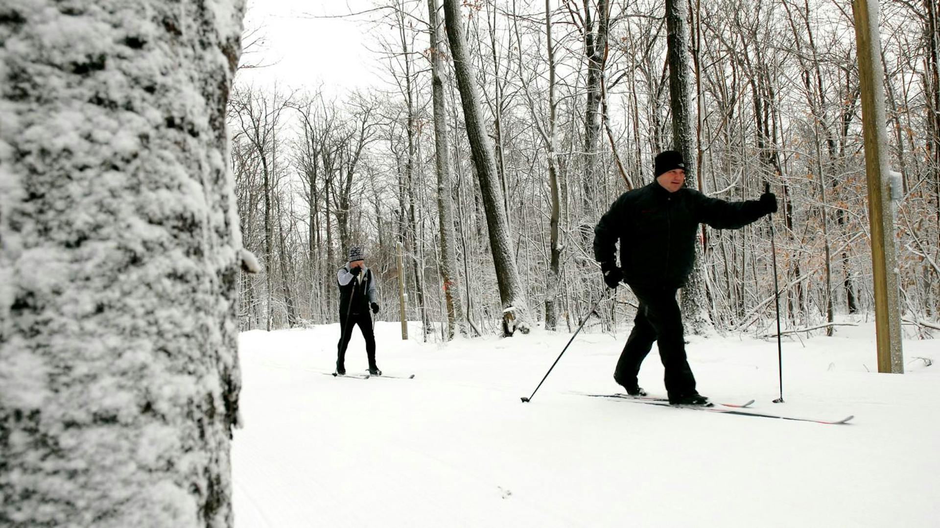 Two male skiers in black ski attire partaking in Nordic skiing at Bristol Mountain in New York, USA. 