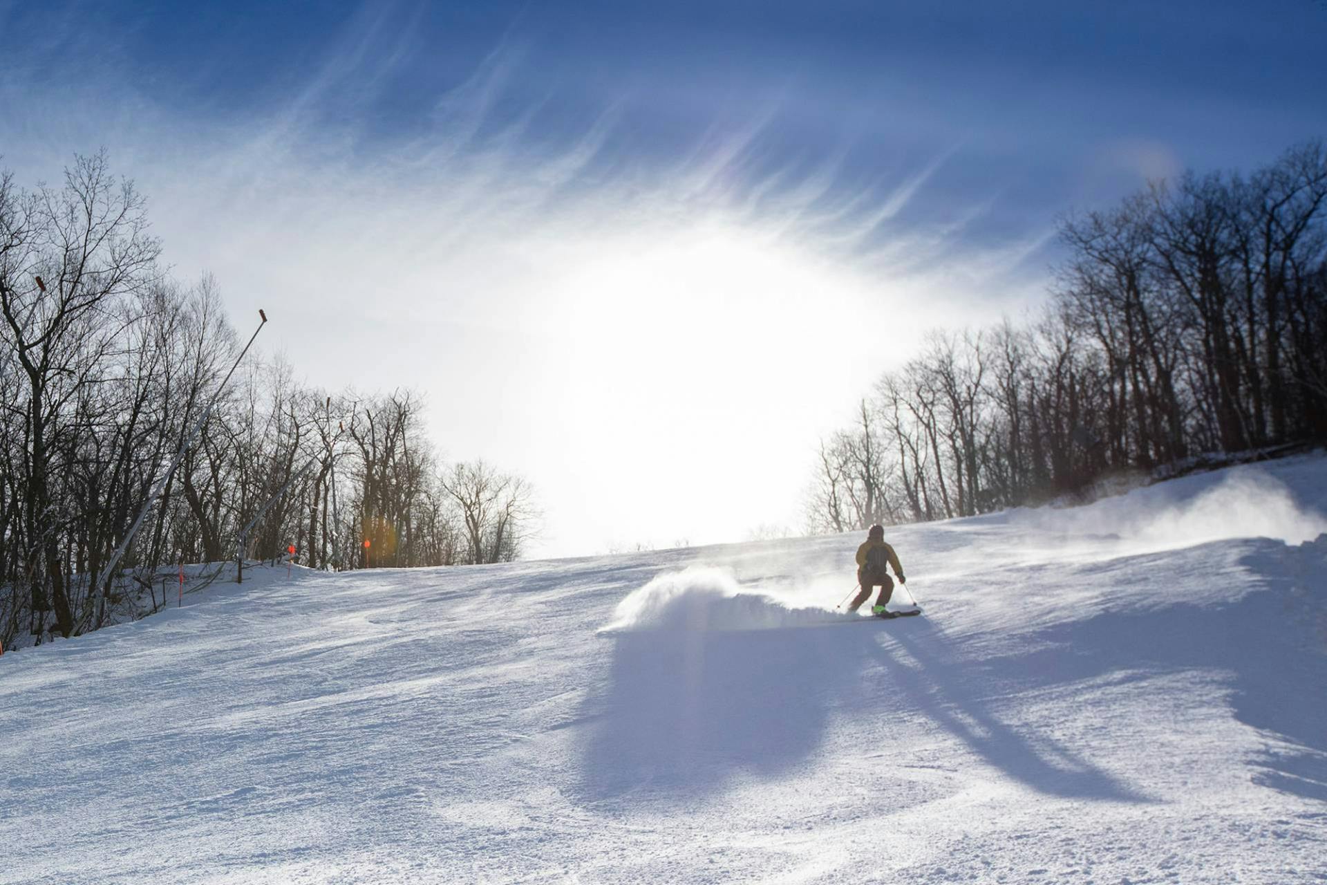 Skier of undiscernible gender in yellow and black ski attire hitting the slopes at Catamount in New York, USA.
