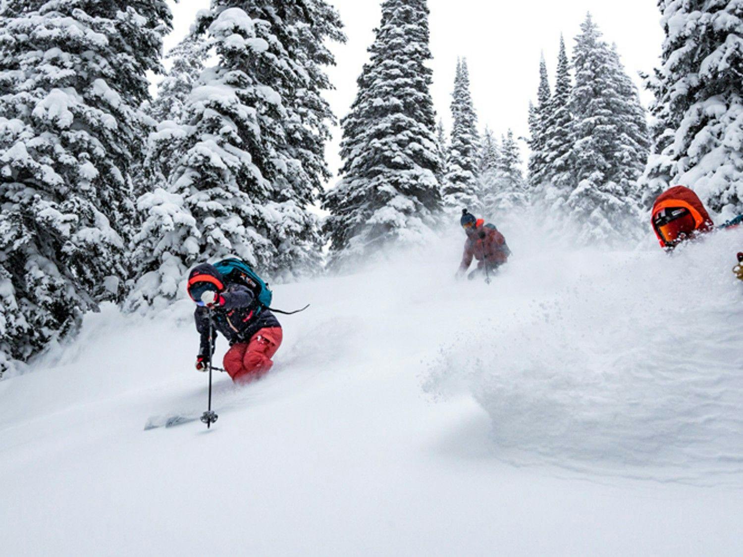 Three skiers of undiscernible gender in orange and black ski attire hitting the slopes at Kirkwood near Lake Tahoe in California, USA.