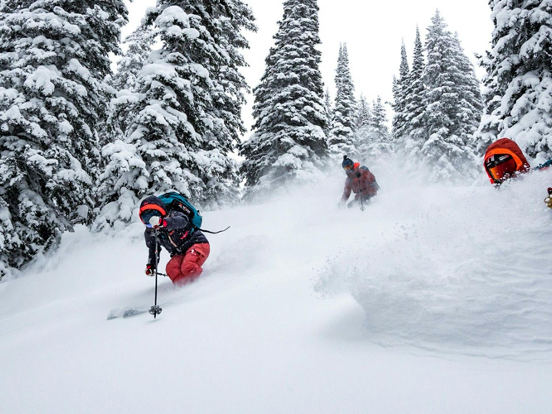 Three skiers of undiscernible gender in orange and black ski attire hitting the slopes at Kirkwood near Lake Tahoe in California, USA.