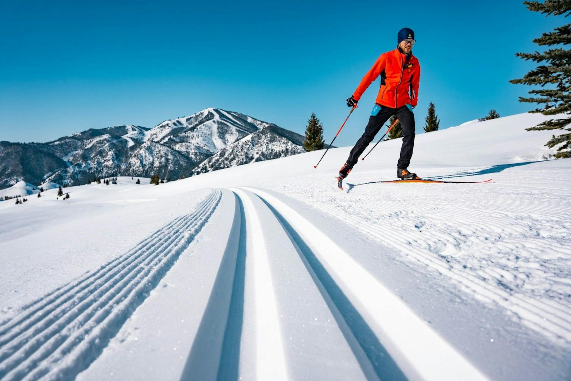 Male skier in red-orange ski jacket and black ski pants engaging in Nordic skiing at Sun Valley in Idaho, USA.